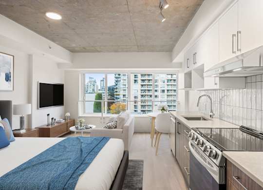 A modern living space with a large bed, a sofa, a flatscreen television, and a kitchen area.