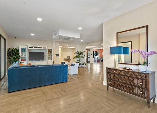 A blue couch sits in a spacious living room with a wooden floor and a large mirror on the wall.