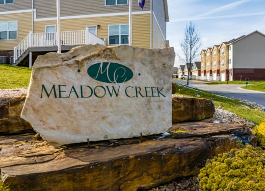 a stone sign that reads meadow creek in front of houses
