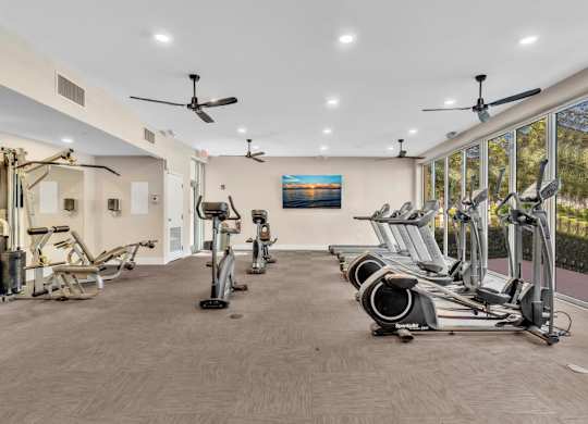 A gym with a variety of exercise equipment including treadmills, stationary bikes, and elliptical machines.