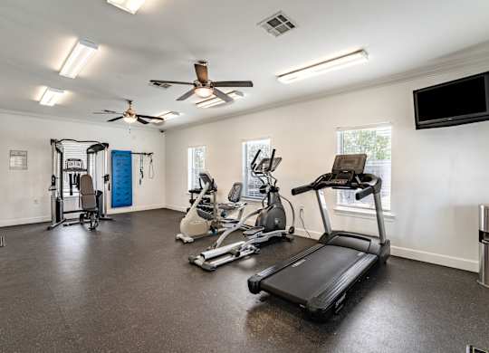 A spacious home gym with a treadmill, elliptical machines, and a fan.