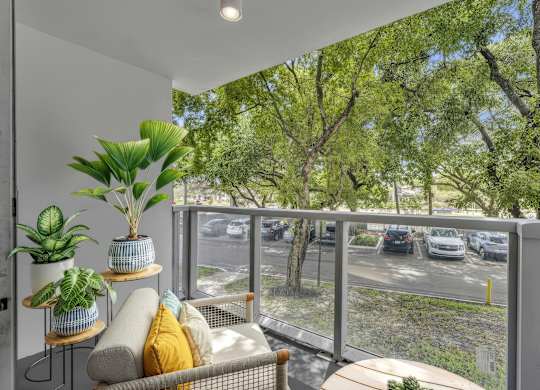 A balcony with a couch, plants, and a view of a parking lot.