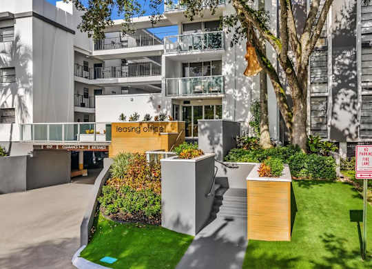 A leasing office is located in a modern building with a landscaped area in front.