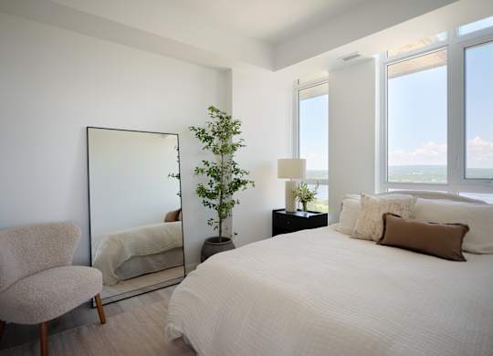 A bedroom with a large bed, a chair, a mirror, and a potted plant.