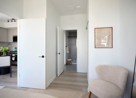 A white chair sits in a hallway with a white door and a picture on the wall.