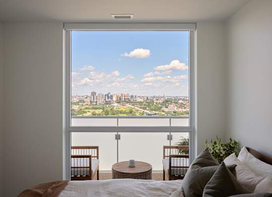 A bedroom with a large window overlooking a cityscape.