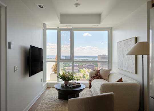 A living room with a flat screen TV mounted on the wall and a large window with a view of the city.