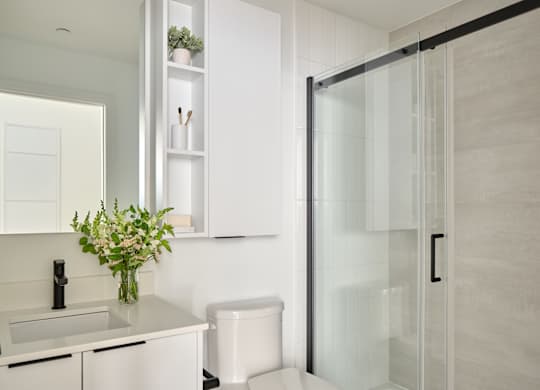 A white toilet sits in a modern bathroom next to a sink and a glass shower door.