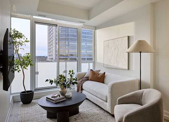 A living room with a grey couch, a black table, a plant, a lamp, and a painting on the wall.