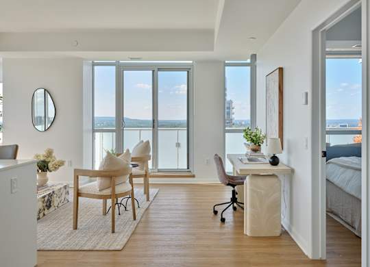 A room with a desk, chairs, and a view of the city through the windows.
