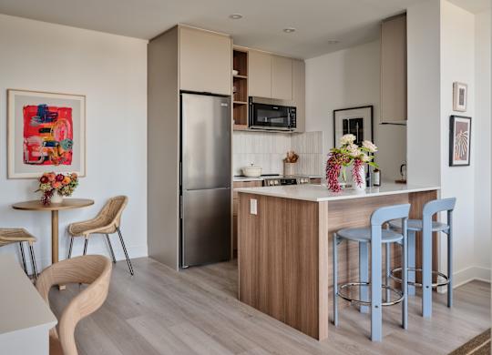 A kitchen with a refrigerator, bar stools, and a dining table with chairs.