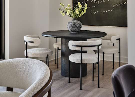 A round table with a vase of flowers on it and chairs around it.