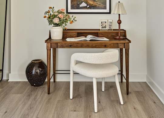 A desk with a chair and a vase with flowers on it.