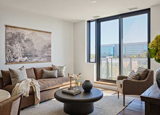 A living room with a large window and a painting on the wall.