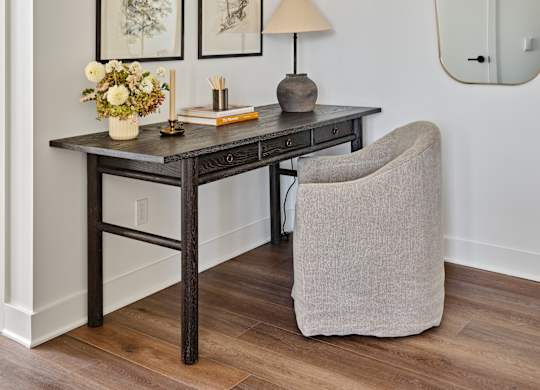 A table with a lamp and flowers on it with a chair in front of it.