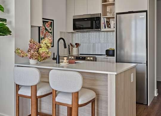 A kitchen with a white countertop and bar stools.