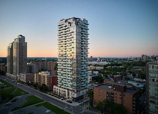A tall, modern glass building stands in the foreground of a cityscape at dusk.