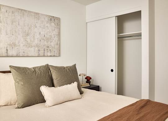 A bed with a brown pillow and a white pillow is in front of a painting.