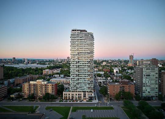 A tall, modern building stands in the middle of a cityscape at dusk.