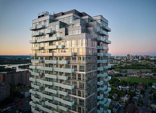A tall, modern building with many windows and balconies is shown from a distance.