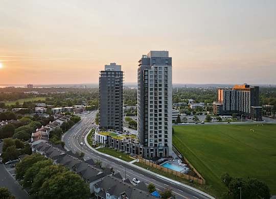 Two tall buildings are situated in a green field with a road running in between them.
