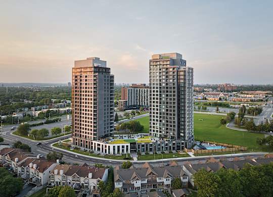 Two tall buildings are surrounded by a green field and smaller buildings.