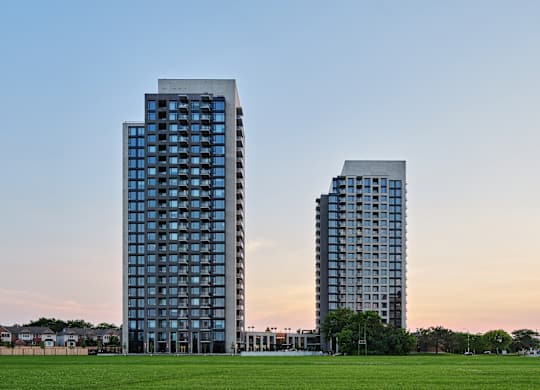 Two modern high-rise buildings with glass windows are situated in a grassy area.