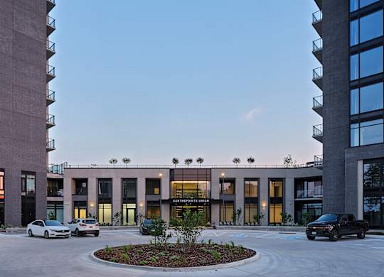 A modern building with a circular garden in front and cars parked outside.