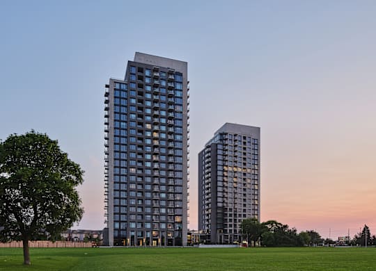 Two modern high-rise buildings are situated in a grassy area with trees.