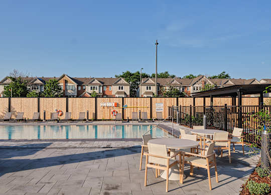 A pool area with chairs and tables in front of a fence and houses.