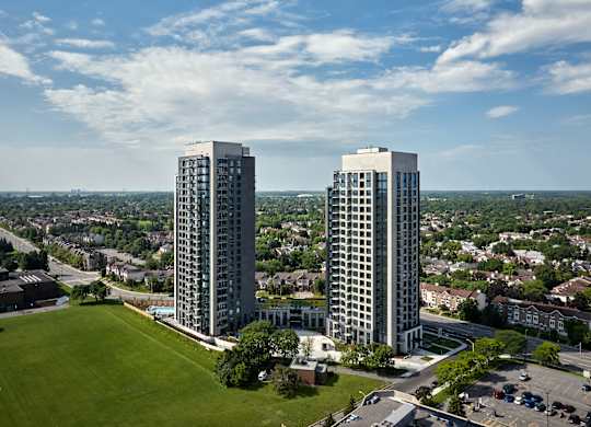 Two tall buildings are surrounded by a green field and a parking lot.
