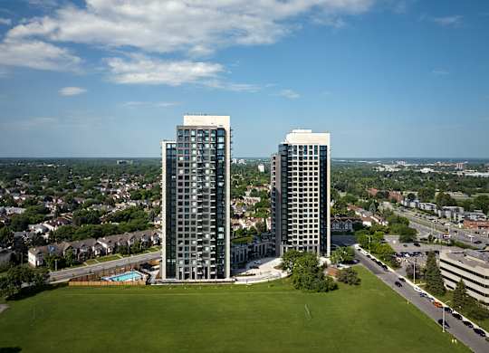 Two tall buildings are surrounded by a green field.