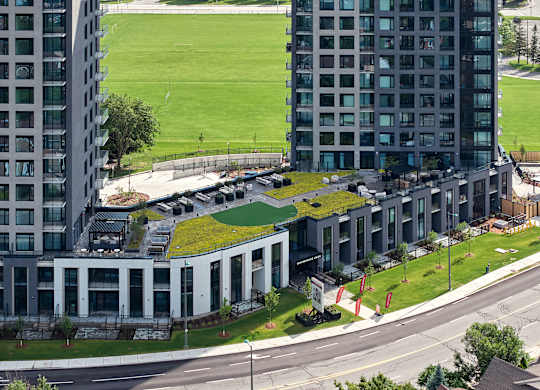 A modern building with a green roof is surrounded by other buildings.