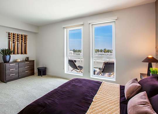 A bedroom with a purple bedspread and a window showing a view of a parking lot.