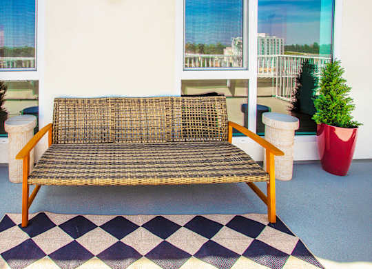 A wicker sofa sits on a checkered rug in front of two red planters.