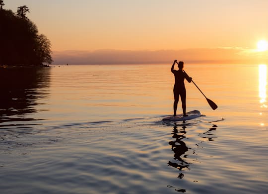 Person paddleboarding on calm water at sunset at Windham Village Apartments, Windham, Maine