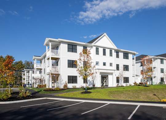 A large white building with a black roof and a parking lot in front.