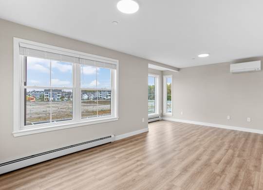 Bright living room with LVP flooring, large windows, and modern climate control.