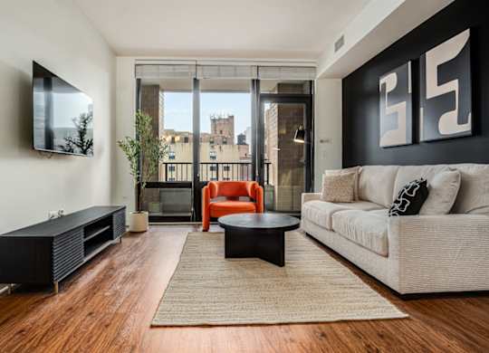 A living room with a white couch, a black coffee table, and a flat screen TV mounted on the wall.