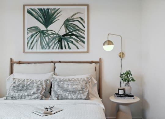 a bedroom with a bed with pillows and a framed picture of plants
