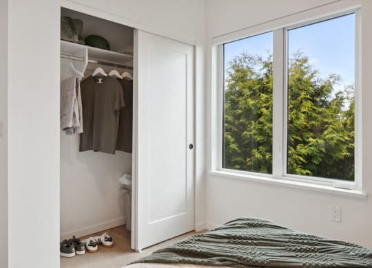 a bedroom with a large window and a closet with clothes