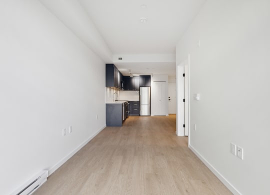 the living room and kitchen of an apartment with white walls and wood floors