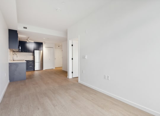 the living room and kitchen of an apartment with white walls and wood floors