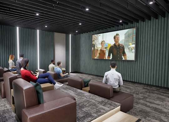 A group of people are sitting in a room with a large screen on the wall.