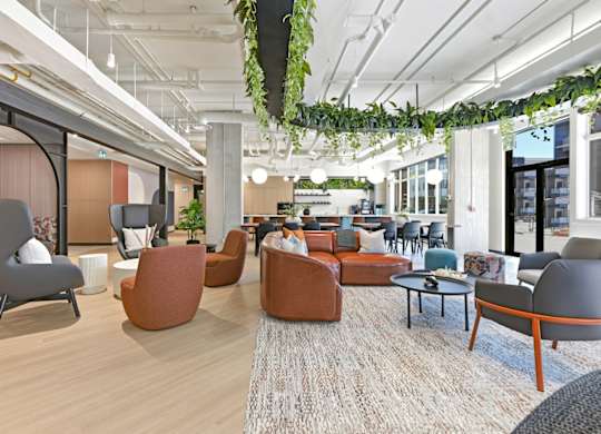 A modern office space with a variety of seating options and plants hanging from the ceiling.