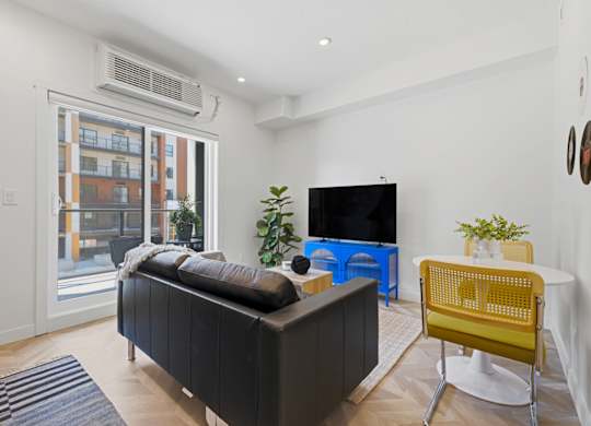 A living room with a black sofa, a yellow chair, and a flat screen TV.