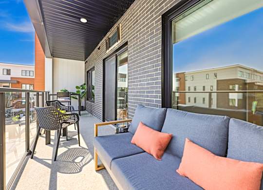 A balcony with a grey couch and orange pillows.