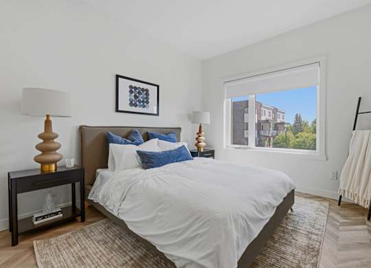 A bedroom with a large bed and a view of a building outside the window.