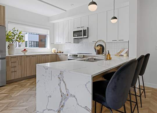 A modern kitchen with a marble island and black chairs.