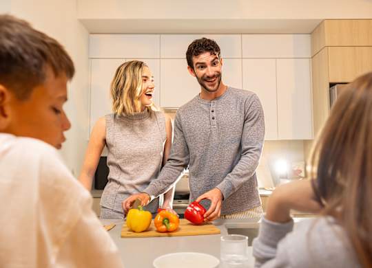 A family of four is preparing food together in the kitchen.